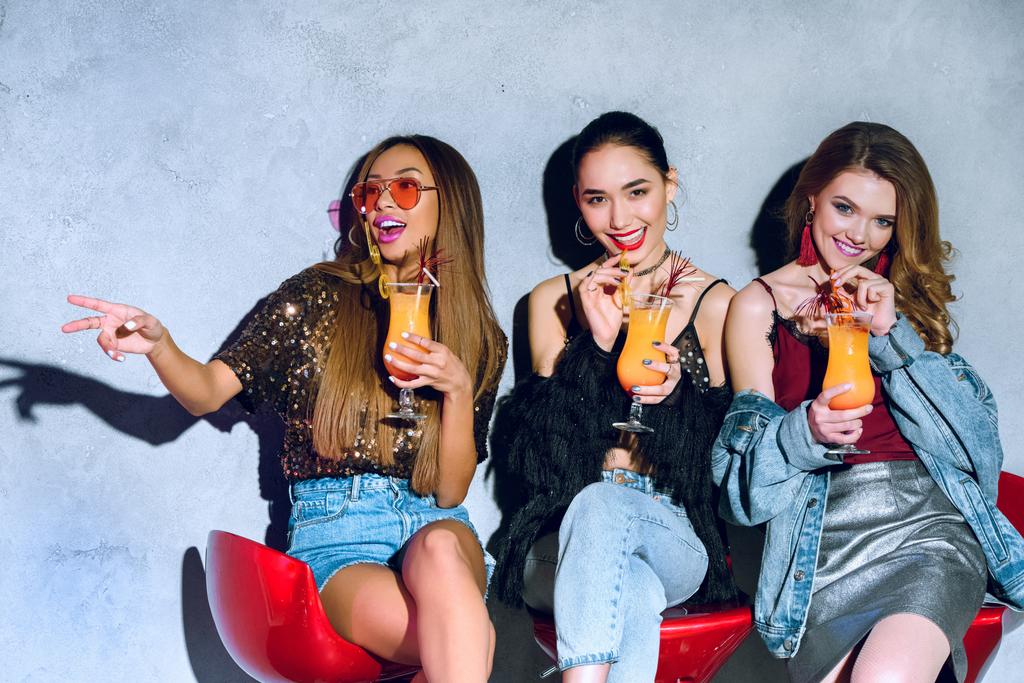 joyeuses filles multiethniques élégantes assises sur des tabourets de bar et buvant des cocktails à la fête
 - Photo, image