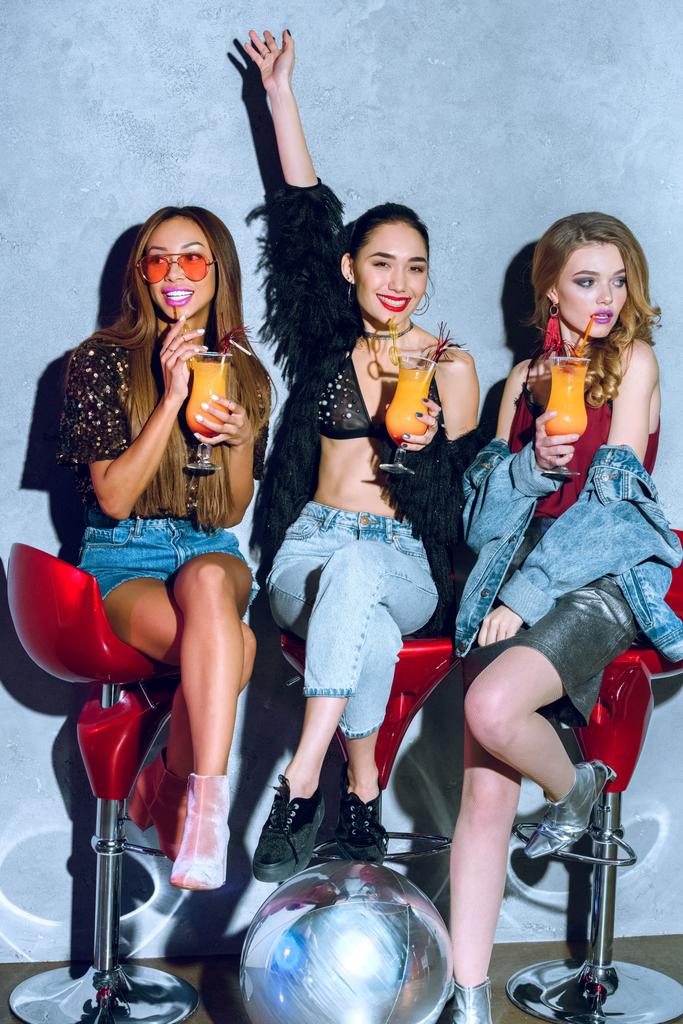 schöne modische multiethnische Frauen sitzen auf Barhockern und trinken Cocktails auf einer Party - Foto, Bild