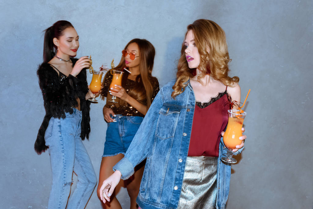 modieuze meisje houdt van glas met cocktail terwijl multi-etnisch vrienden die achter - Foto, afbeelding