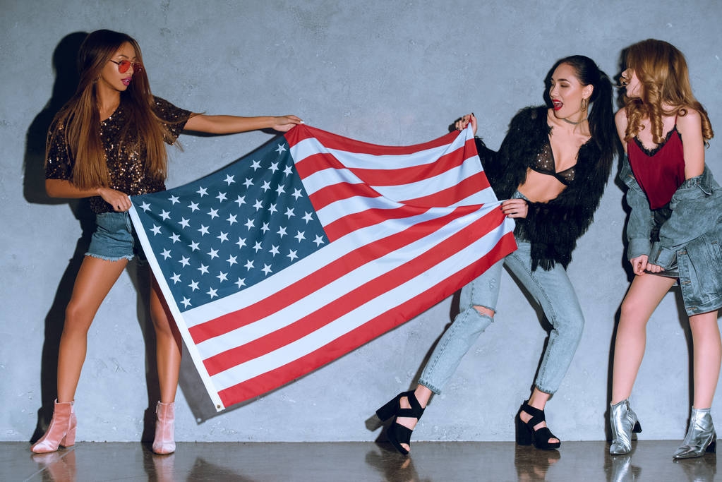 mujeres jóvenes multiculturales con bandera americana contra muro de hormigón
 - Foto, imagen