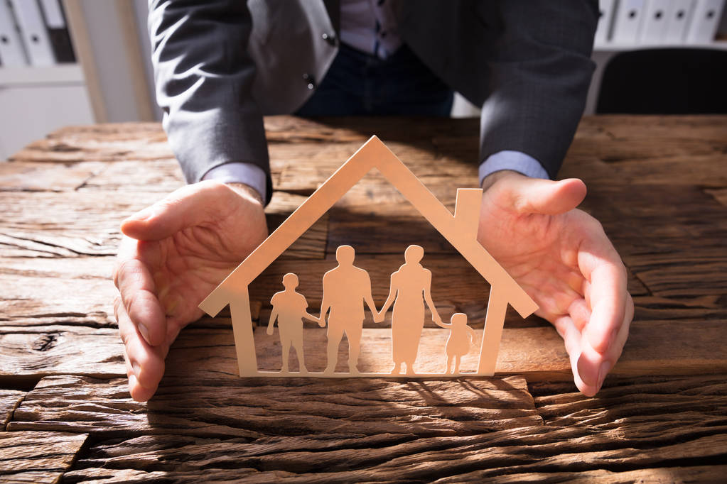 Rukou si podnikatel House Model a rodinné papíru vystřihnout na dřevěné desce - Fotografie, Obrázek