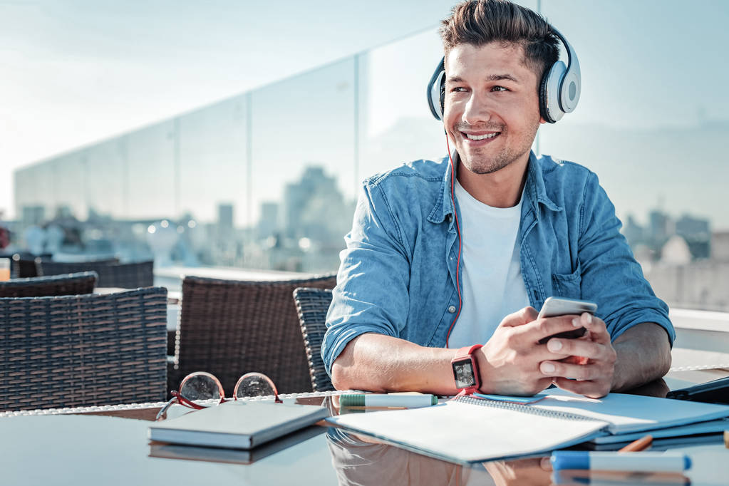 Сияющий молодой человек, сидящий на террасе и слушающий музыку
 - Фото, изображение