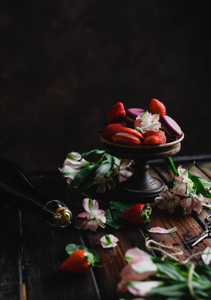 mísa s macarons a jahody na dřevěný stůl s květinami a láhev šampaňského pro Valentýn - Fotografie, Obrázek
