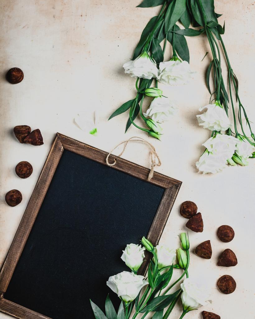 Ansicht der Tafel in Holzrahmen mit Eustoma-Blumen und Schokoladenbonbons - Foto, Bild