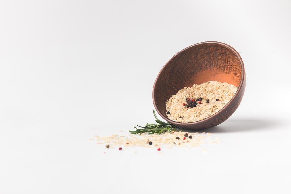 arroz crudo y especias derramando tazón sobre la superficie blanca
 - Foto, Imagen