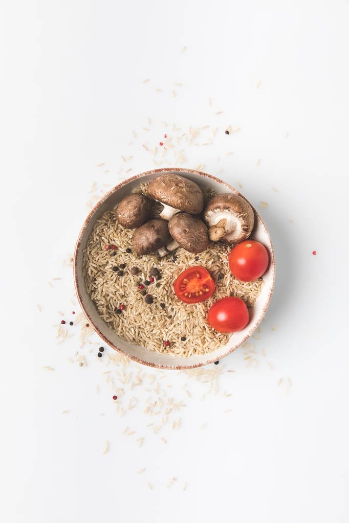 vue du dessus du riz cru dans un bol avec des champignons et des tomates sur la surface blanche avec du riz renversé et des épices autour
 - Photo, image