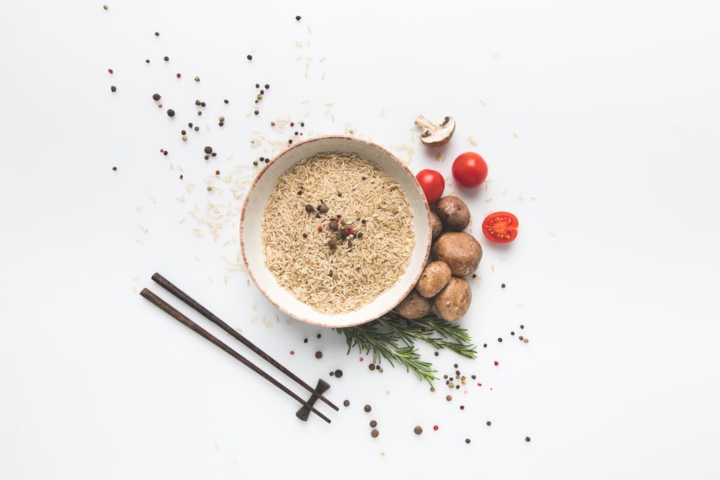flat lay composition of raw rice in bowl with mushrooms and tomatoes on white surface with chopsticks - Photo, Image