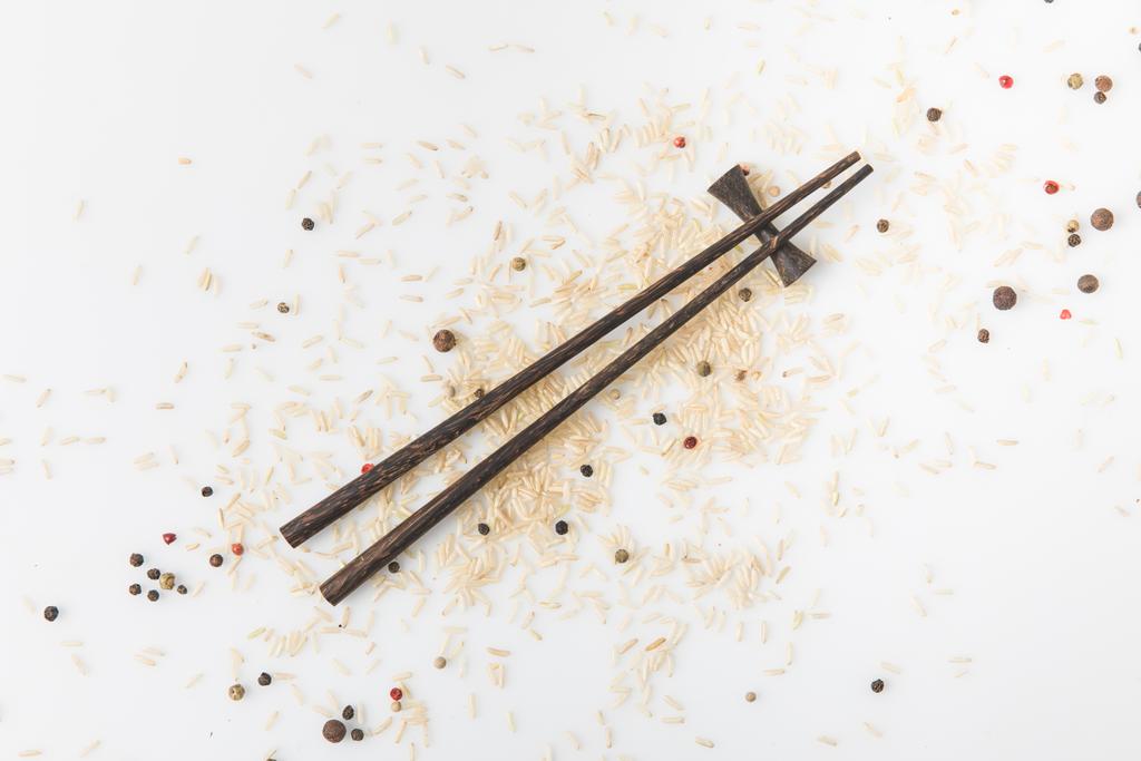 κάτοψη του ακατέργαστο ρύζι και μπαχαρικά χυθεί σε λευκή επιφάνεια με chopsticks - Φωτογραφία, εικόνα