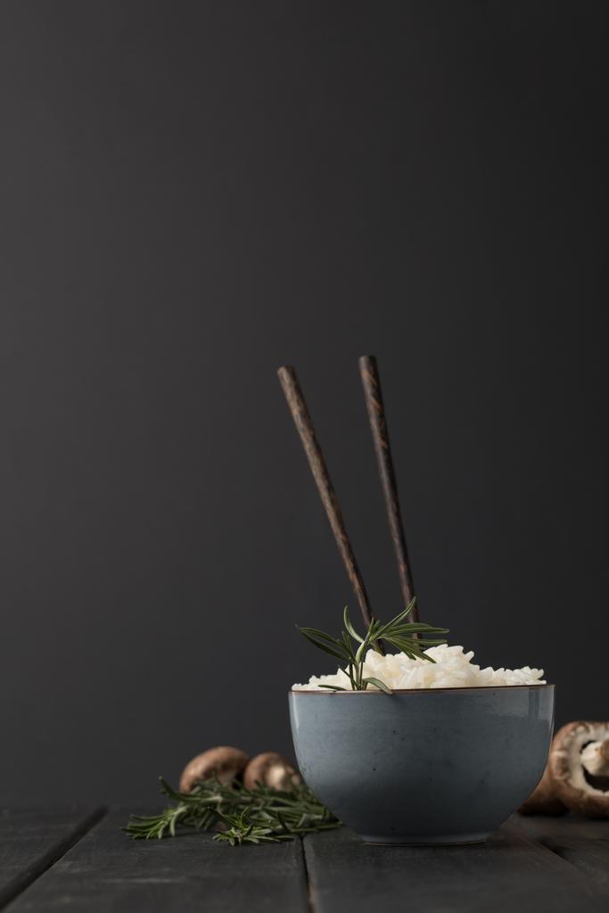 Schüssel mit schmackhaftem Reis mit Stäbchen und Pilzen auf schwarzer Tischplatte - Foto, Bild