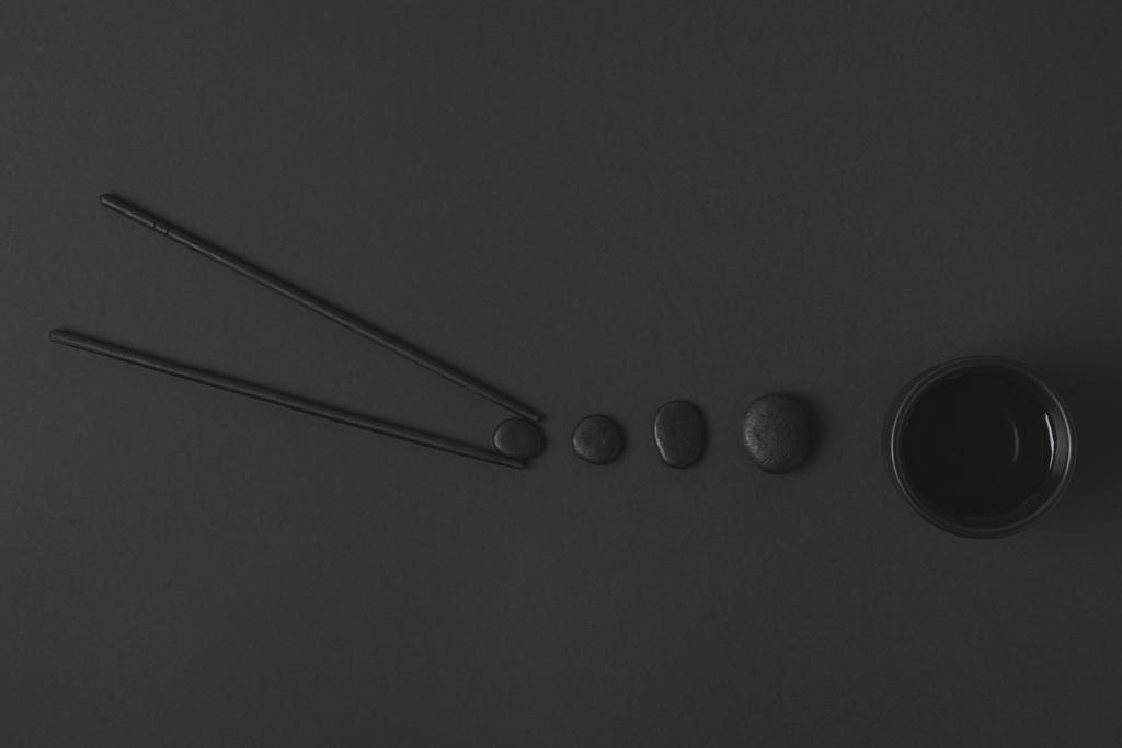 creatieve flat lag samenstelling van chopstick met chinese thee kopje en kiezelstenen op zwart - Foto, afbeelding