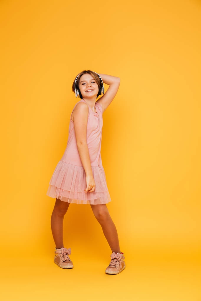 Funny usmívající se dívka v sluchátka představují samostatný nad žlutá - Fotografie, Obrázek