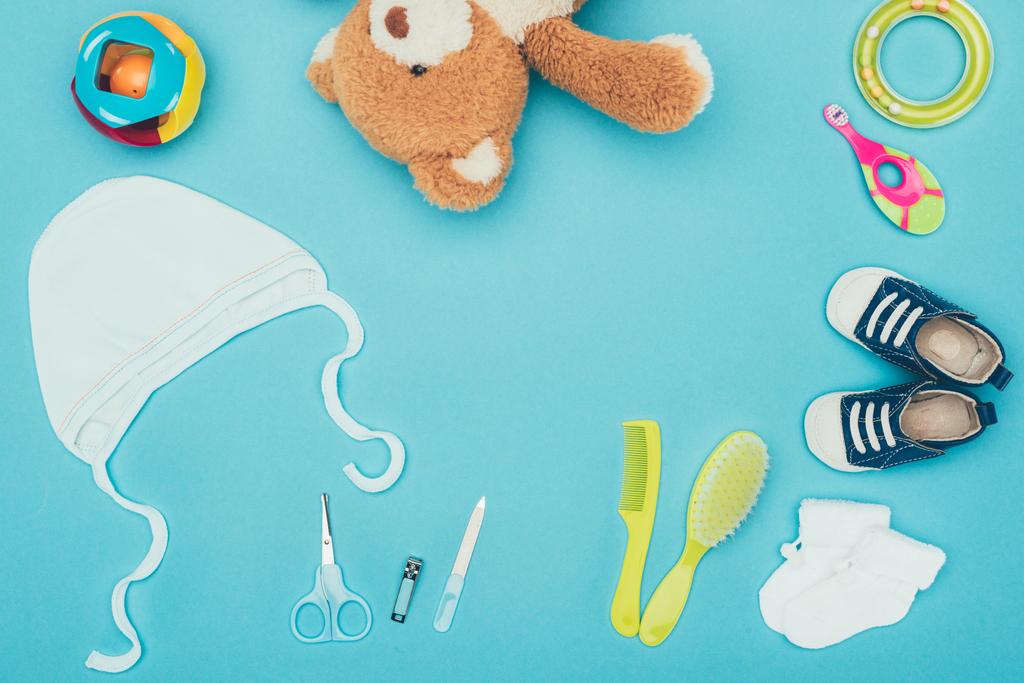 top view of teddy bear and baby clothes with equipment isolated on blue - Photo, Image