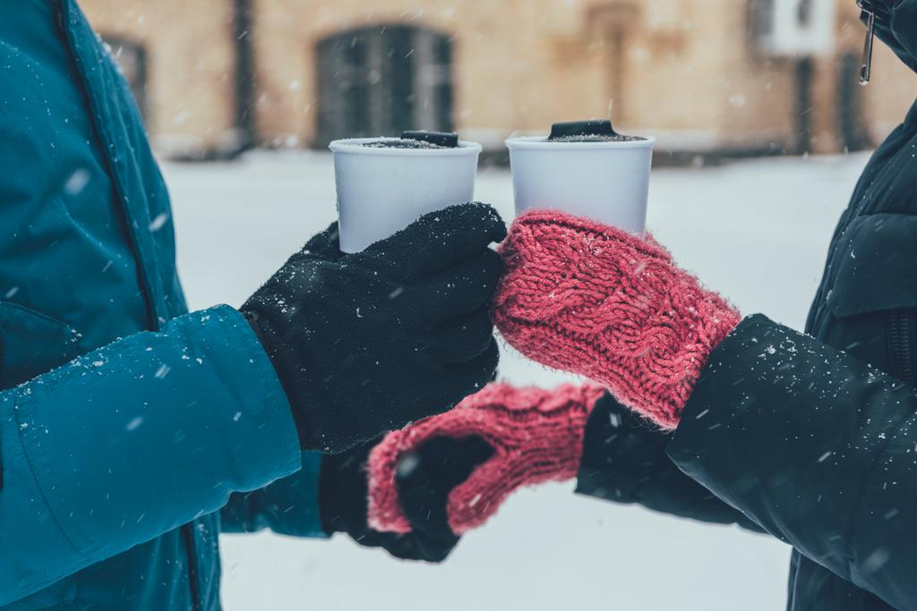 Teilansicht eines Pärchens mit heißen Getränken, das sich im Winter auf der Straße an den Händen hält - Foto, Bild