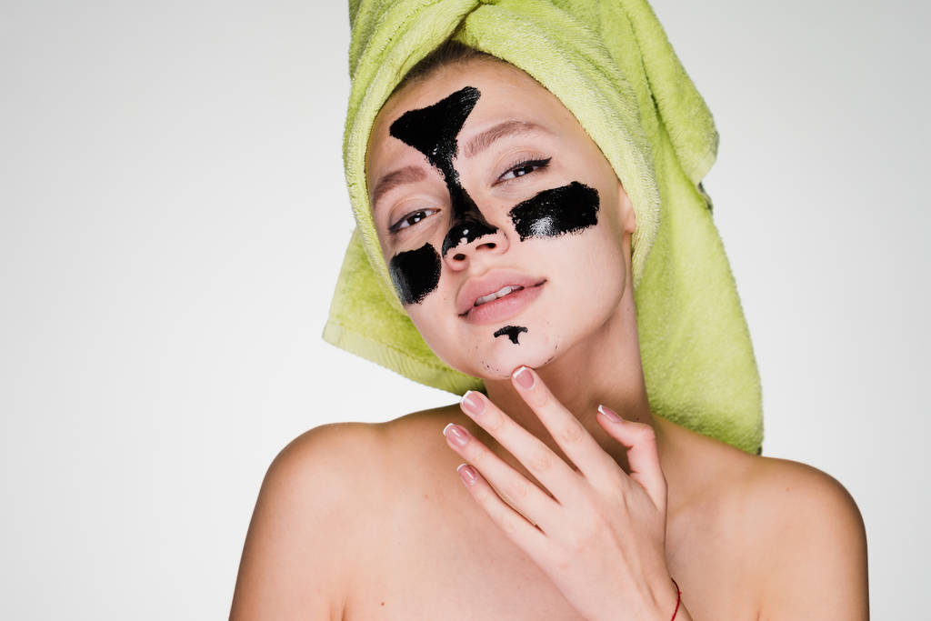 彼女の頭の上のタオルを持つ女性は、問題領域に顔の皮膚をきれいにする黒マスクを適用 - 写真・画像