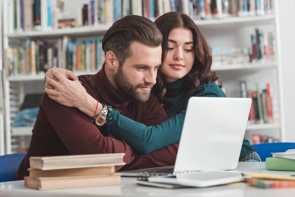 novia abrazando novio y mirando a la computadora portátil en la biblioteca
 - Foto, imagen