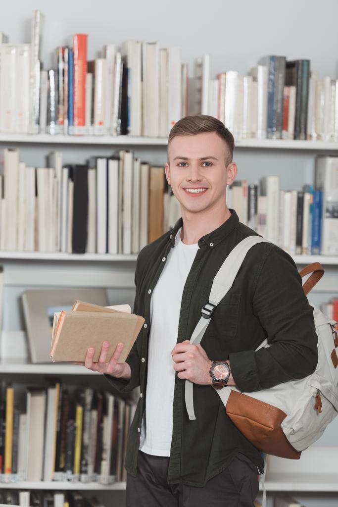 uśmiechnięty mężczyzna student z książki patrząc na kamery w bibliotece - Zdjęcie, obraz