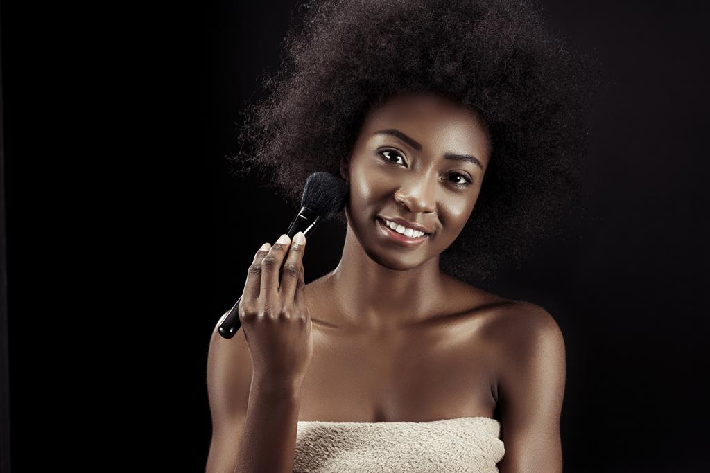 attractive african american woman doing makeup with brush isolated on black - Photo, Image