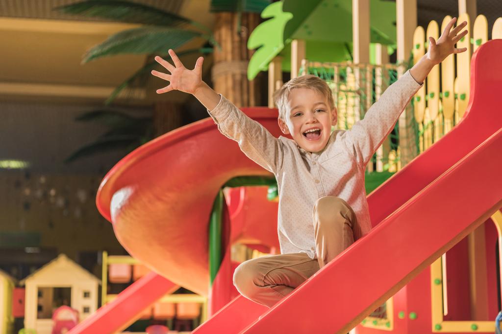 щасливий маленький хлопчик посміхається на камеру, граючи на слайді в розважальному центрі
  - Фото, зображення