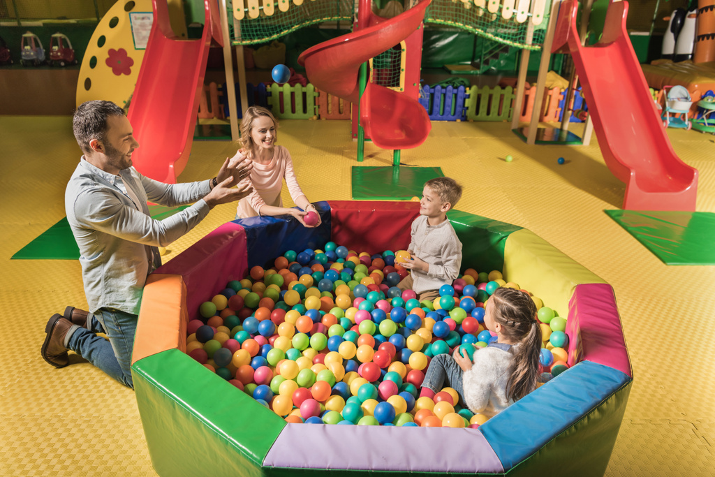 pohled z vysokého úhlu šťastná rodina s dvěma rozkošné děti hrát si s barevnými míčky v zábavním centru  - Fotografie, Obrázek