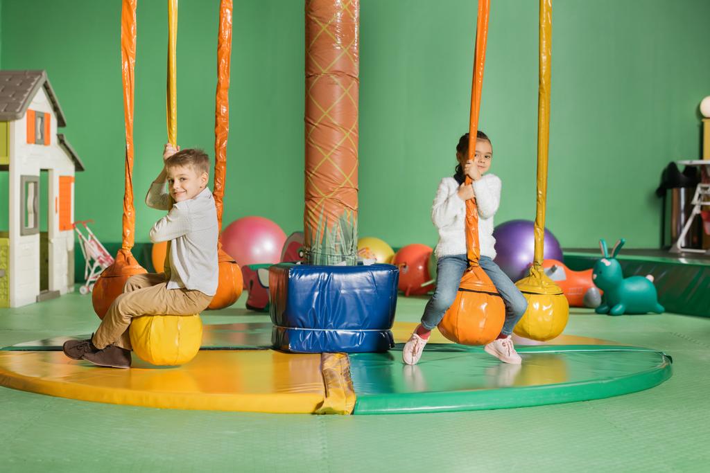 adorável sorrindo irmãos balançando e jogando no centro de entretenimento
 - Foto, Imagem