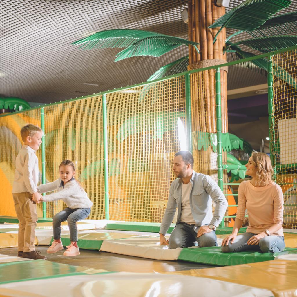 родители смотрят на милых маленьких детей, играющих вместе в развлекательном центре
 - Фото, изображение