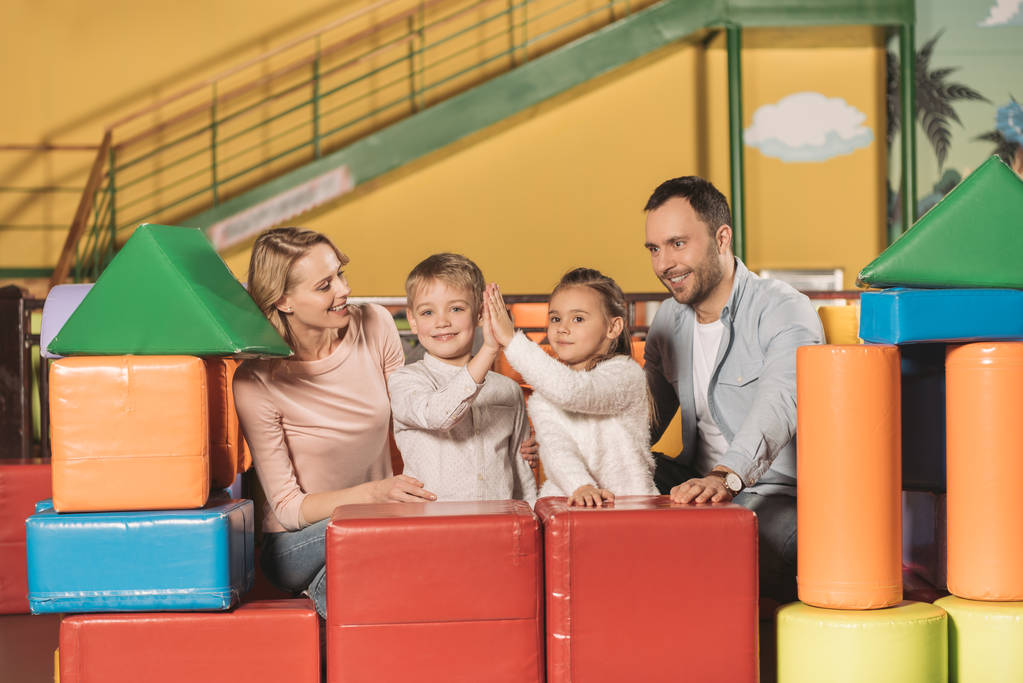glückliche Eltern, die ihre Kinder mit High Five anschauen und im Unterhaltungszentrum in die Kamera lächeln - Foto, Bild