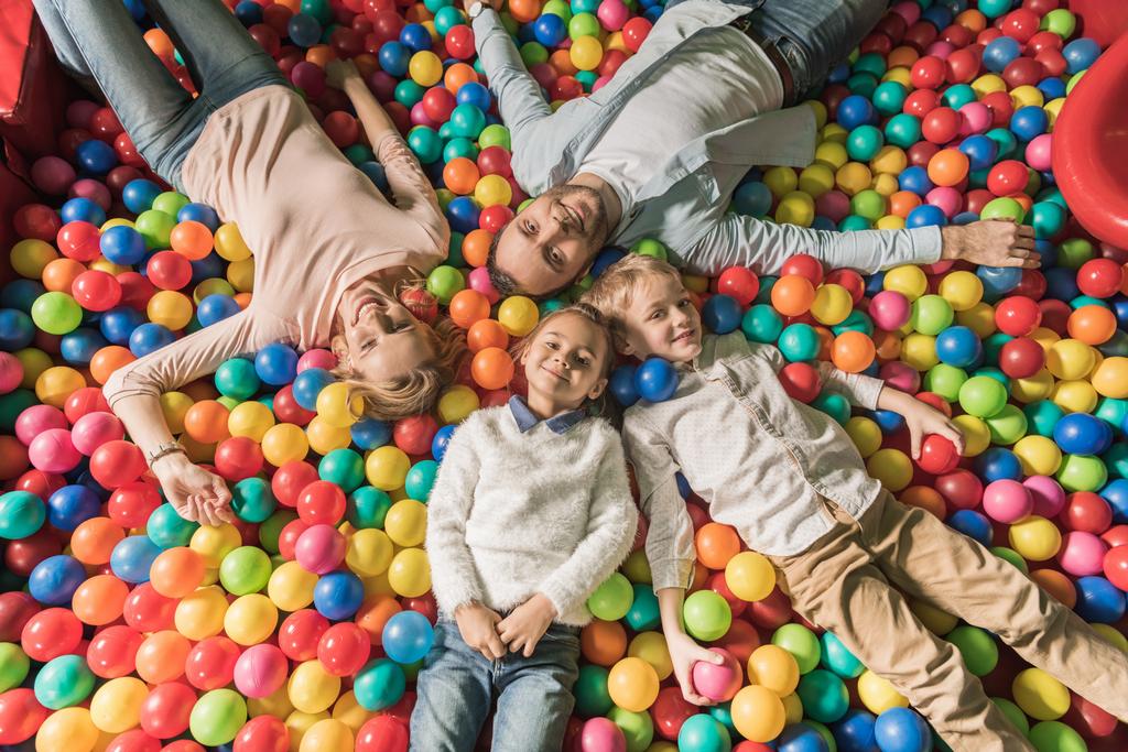 Widok z góry szczęśliwe rodziny z dwójką dzieci, uśmiechając się aparatu podczas leżenia w basenie z kolorowych kulek    - Zdjęcie, obraz