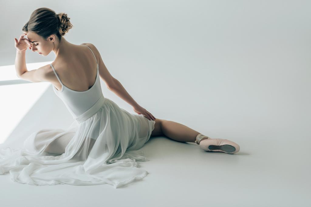 πίσω όψη του κομψό μπαλαρίνα κάθεται σε λευκό φόρεμα και μπαλέτο παπούτσια - Φωτογραφία, εικόνα