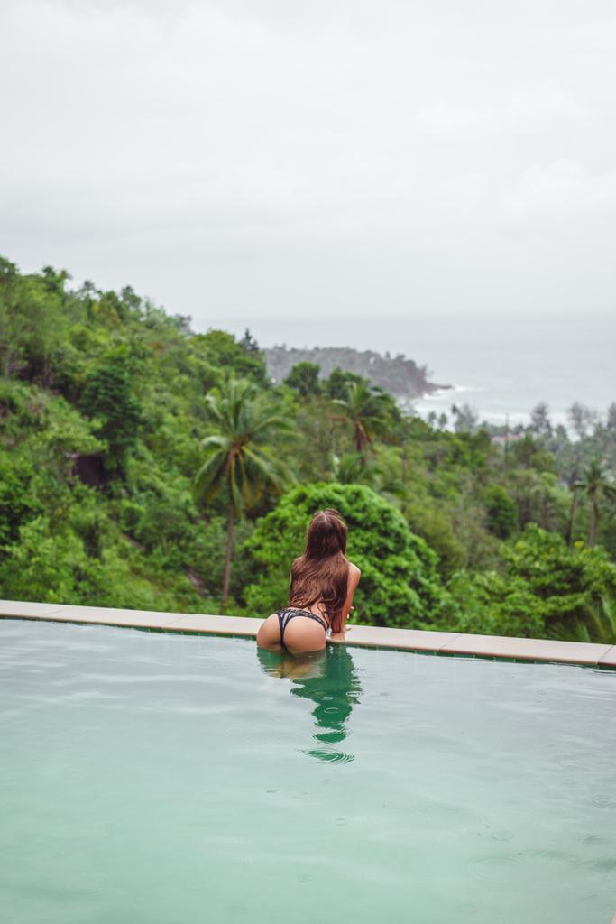 vista trasera de la niña posando en la piscina en el complejo tropical
 - Foto, imagen