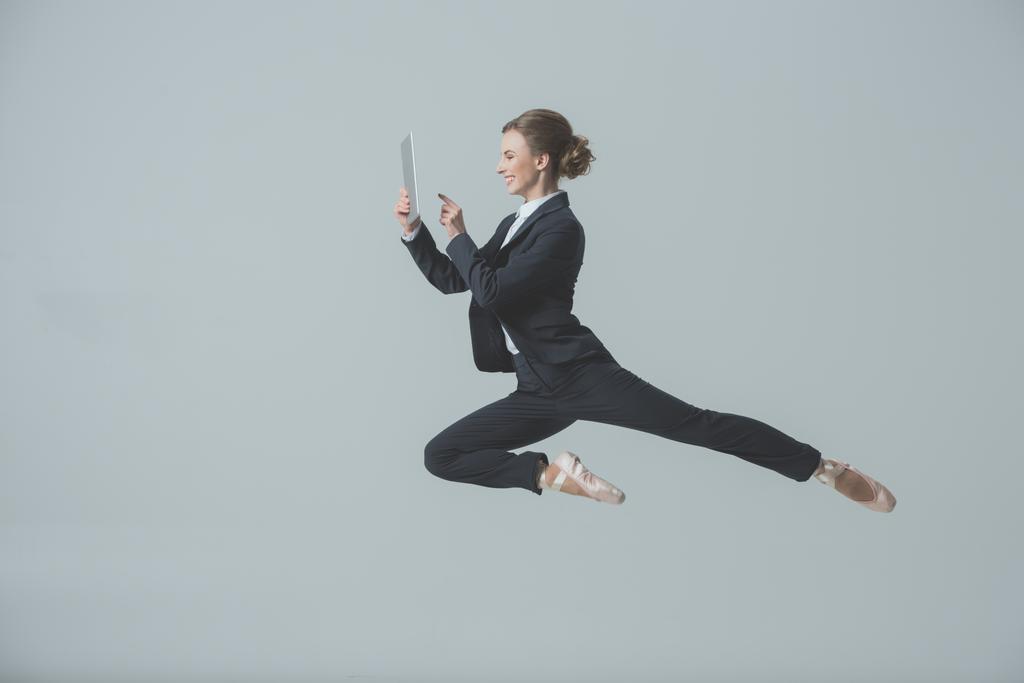 деловая женщина в костюме и балетной обуви прыгать и с помощью цифрового планшета, изолированные на сером
 - Фото, изображение