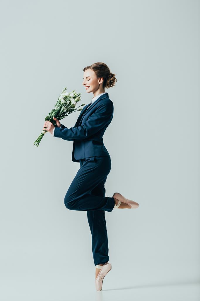 happy businesswoman in suit and ballet shoes with bouquet of flowers, isolated on grey - Photo, Image