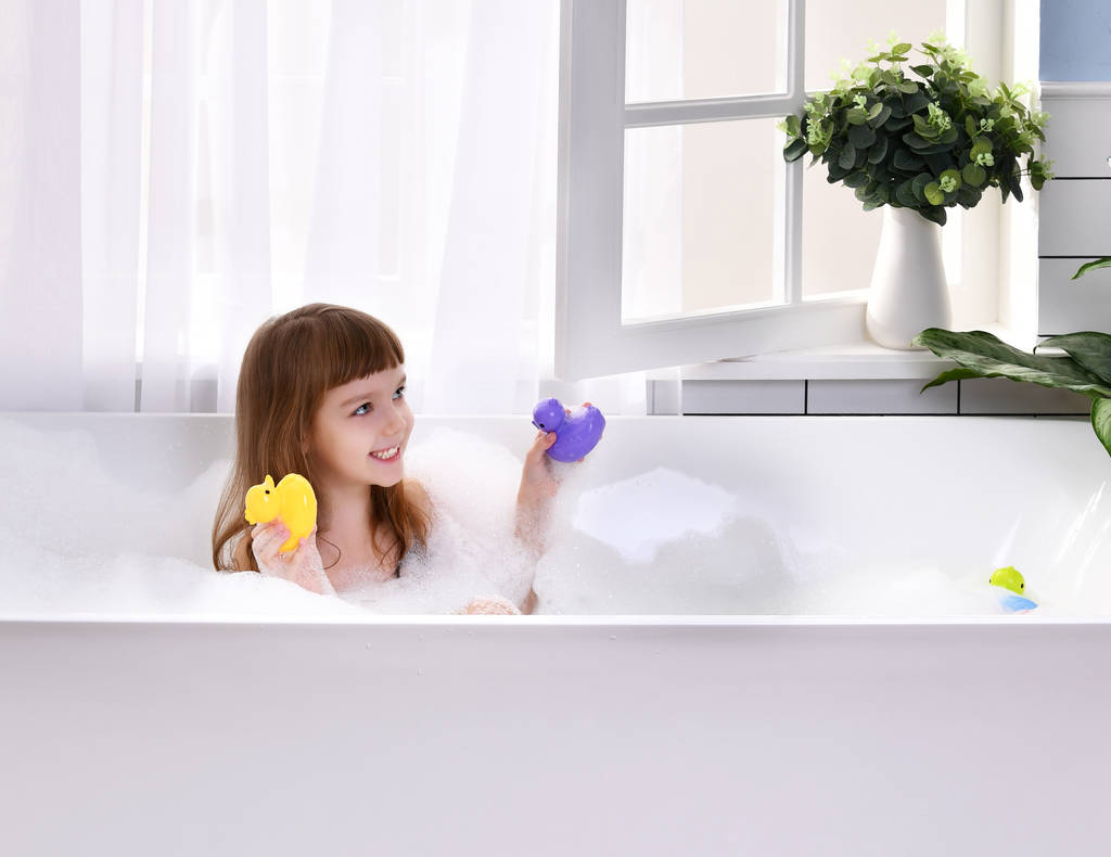  Happy little dziewczynka siedzi w wannie, bawi się zabawkami kaczka w łazience - Zdjęcie, obraz