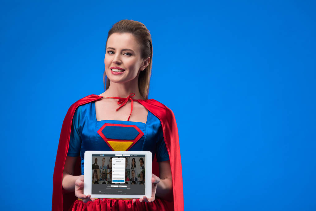 retrato de mulher alegre em traje de super-herói mostrando tablet isolado em azul
 - Foto, Imagem