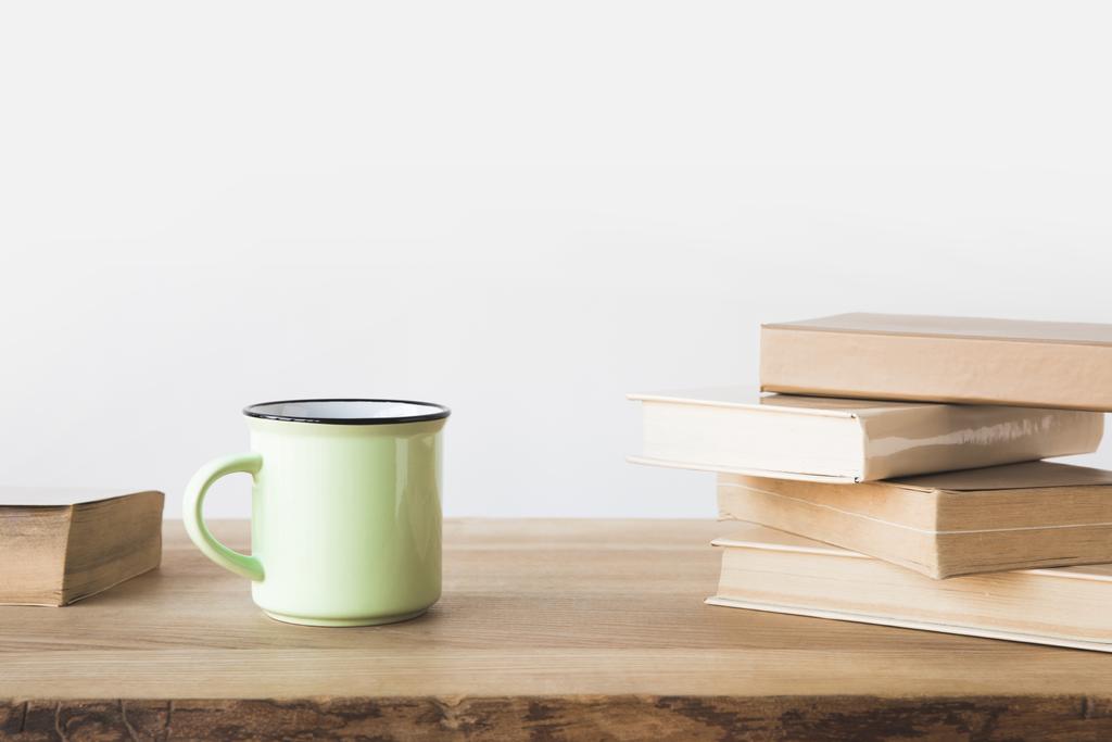 зелена чашка і книги на дерев'яному столі на білому
  - Фото, зображення