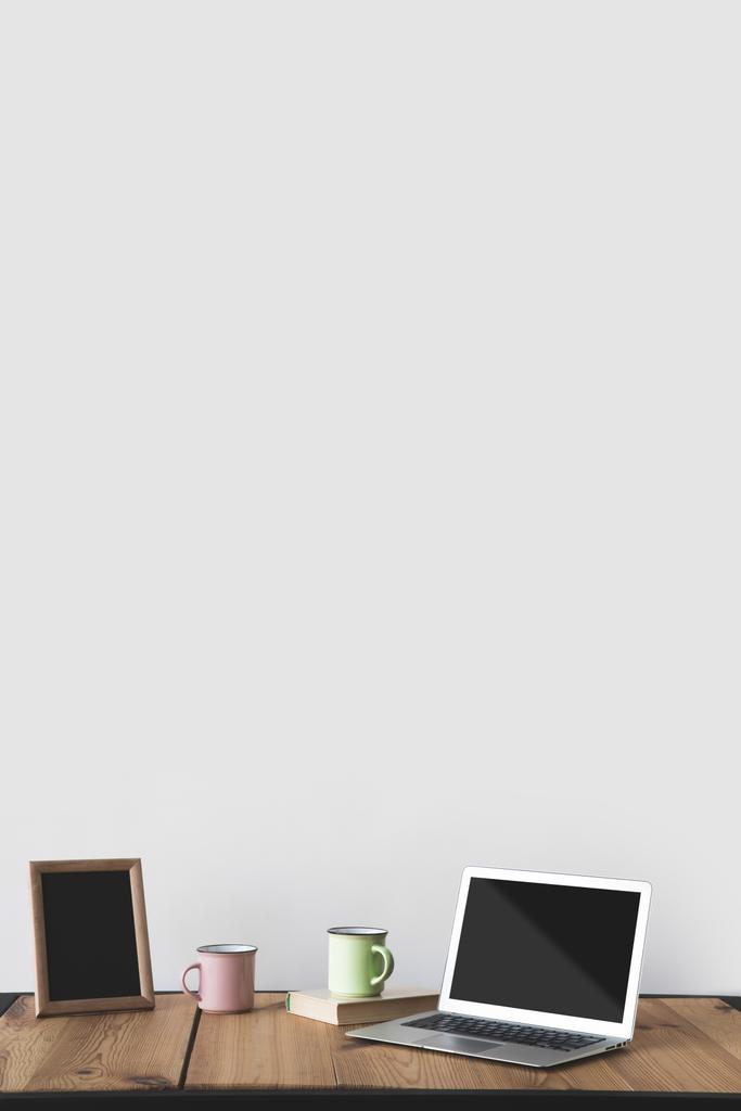 άδειο μαυροπίνακα σε πλαίσιο με κύπελλα και laptop σε λευκό  - Φωτογραφία, εικόνα