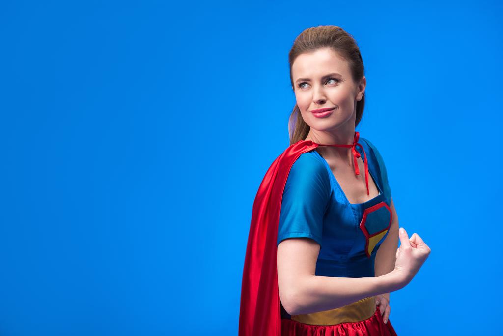 портрет задумчивой женщины в костюме супергероя, показывающий мускулы, изолированные на голубом
 - Фото, изображение