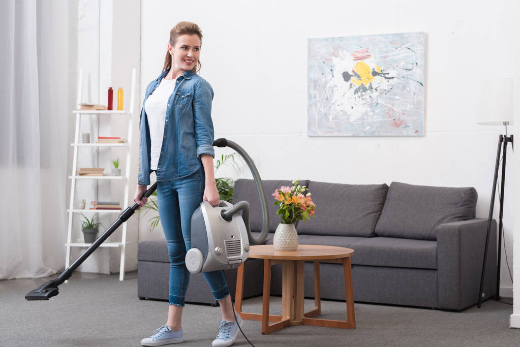 smiling woman with vacuum cleaner in hands looking away - Photo, Image