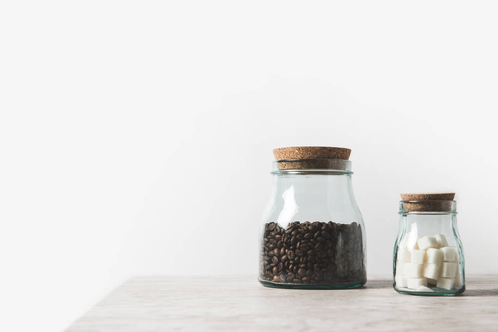 grãos de café e açúcar refinado em garrafas de vidro na mesa de mármore em branco
  - Foto, Imagem