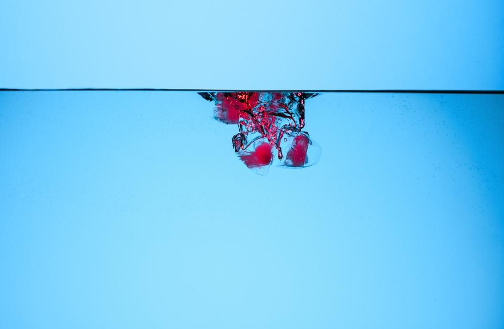 glaçons aux cerises dans l'eau, isolés sur bleu
 - Photo, image