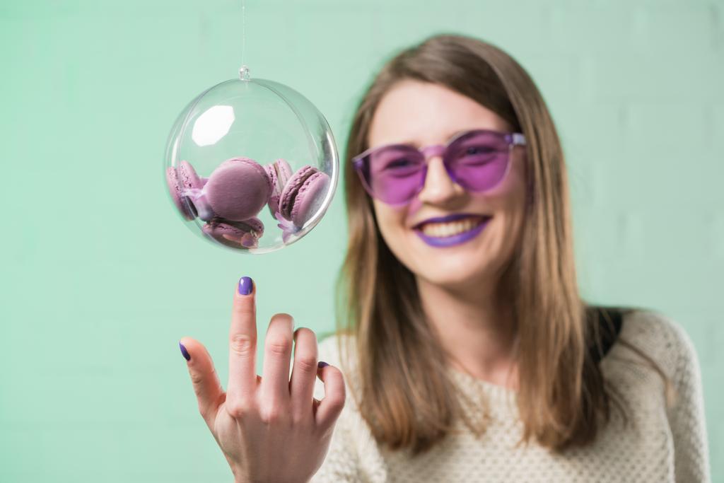 happy young woman in pink eyeglasses touching glass ball of macarons - Photo, Image