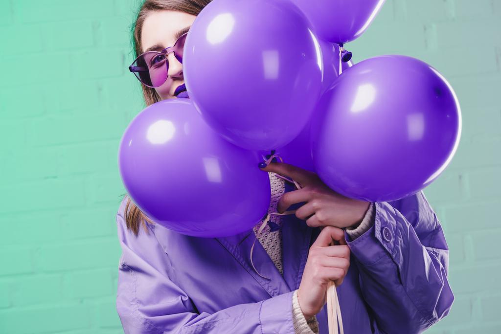 young woman in sunglasses hiding behind purple balloons - Photo, Image