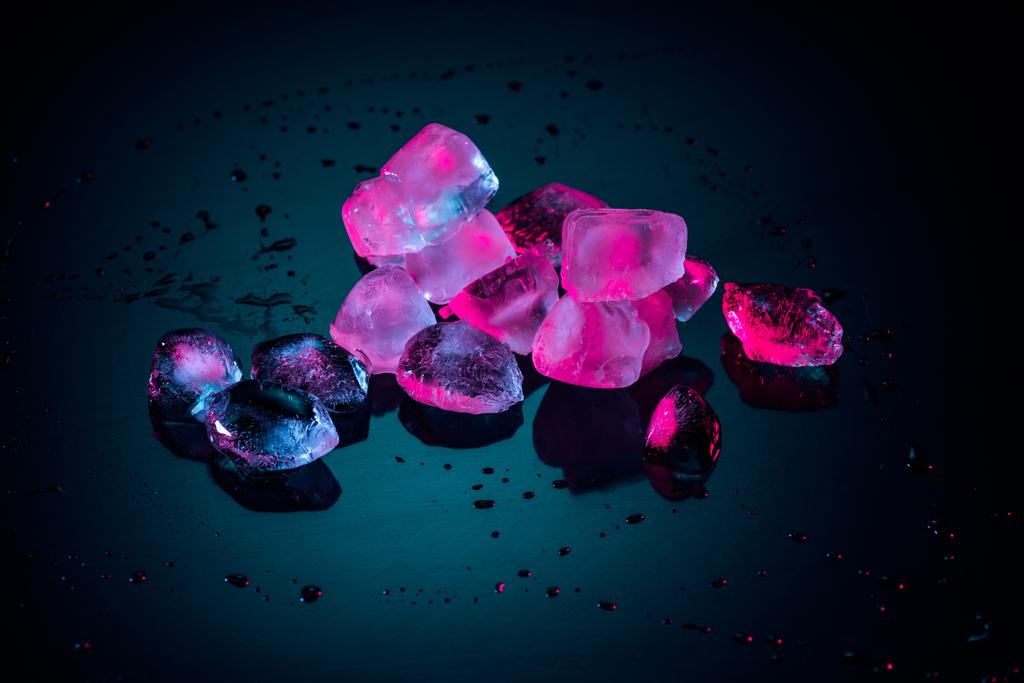 close up de cubos de gelo rosa derretendo em preto com gotas
 - Foto, Imagem
