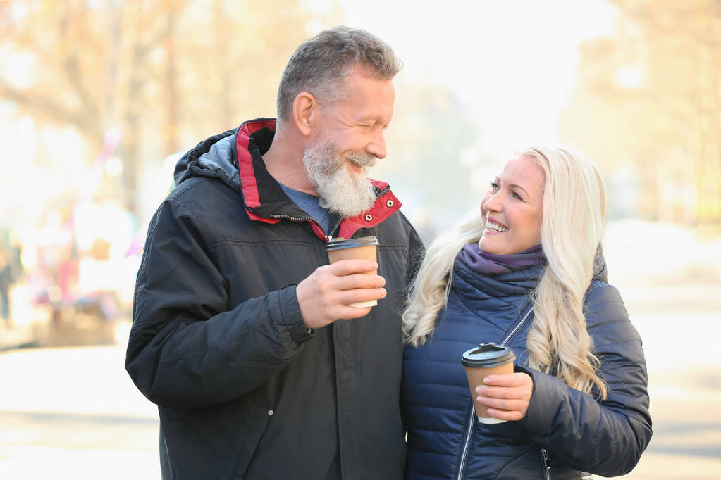glückliches älteres Paar, das an einem Herbsttag auf der Straße spaziert und Kaffee trinkt - Foto, Bild