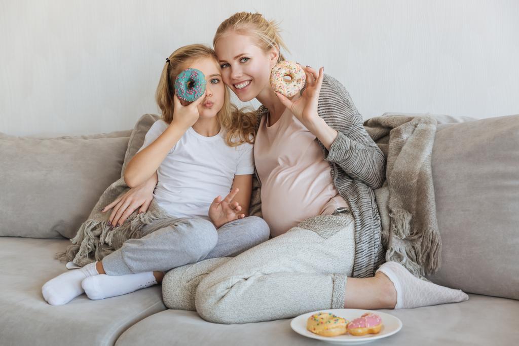 幸せな妊娠中の母親と娘のドーナツを楽しんで - 写真・画像