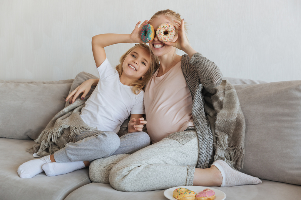 glückliche schwangere Mutter und Tochter bedecken Augen mit Donuts - Foto, Bild