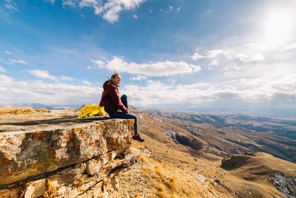 Touristin sitzt am Rand der Klippe vor dem Hintergrund der Berge - Foto, Bild