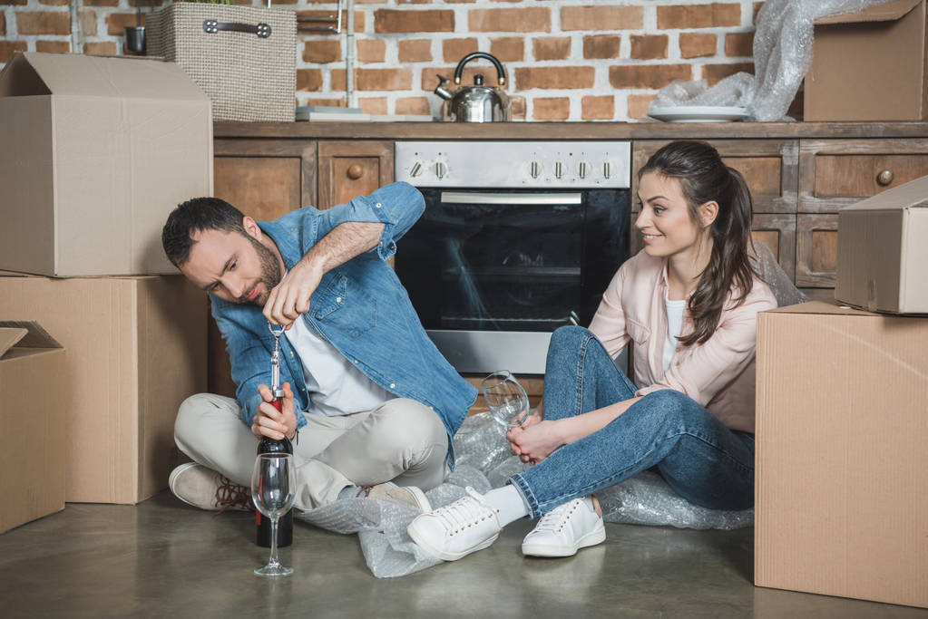 glückliches junges Paar öffnet Flasche Wein und feiert Umzug in neuer Wohnung - Foto, Bild