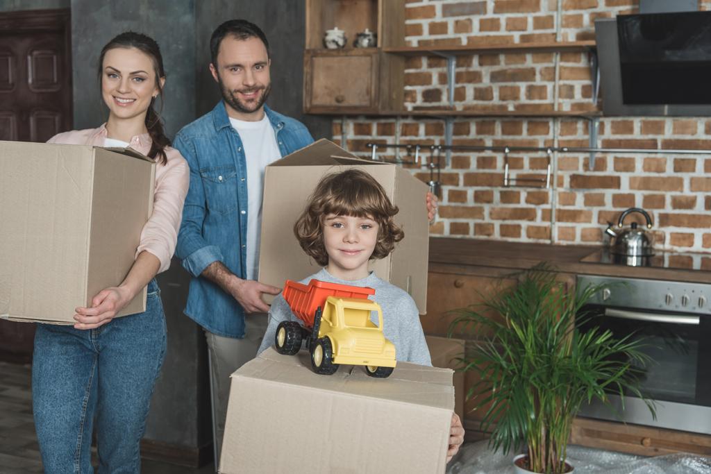 šťastná rodina drží kartonových krabic a usmívá se na kameru při přemístění - Fotografie, Obrázek