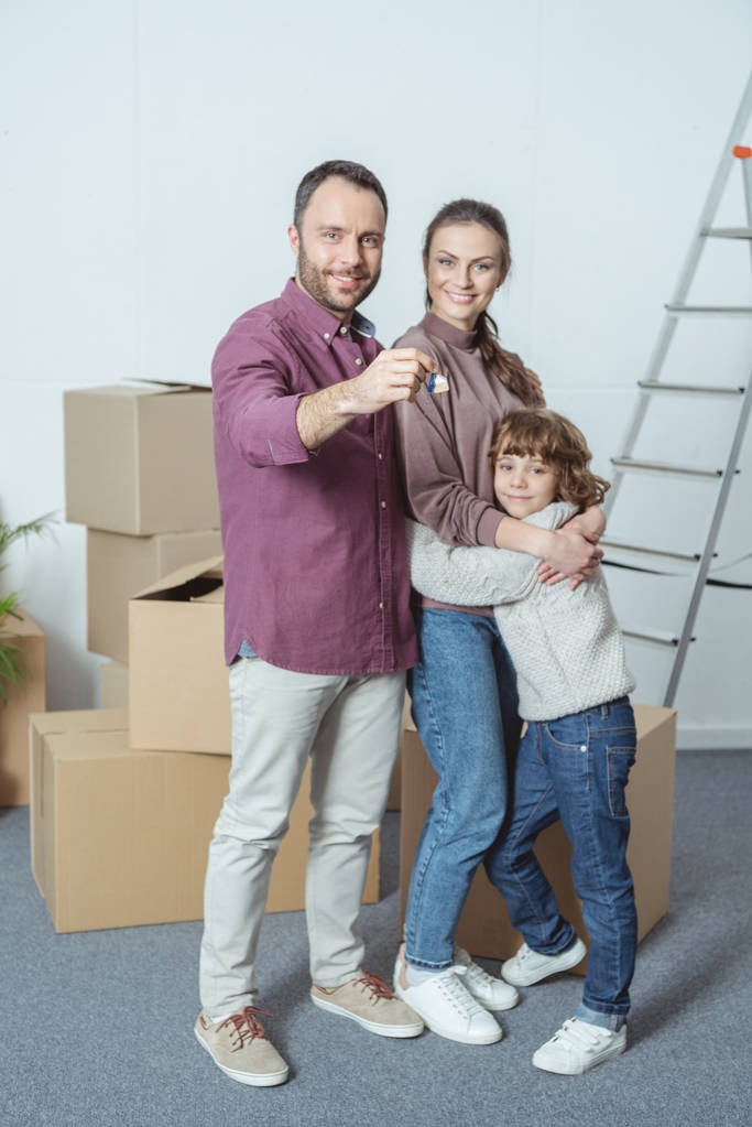 ευτυχισμένη οικογένεια με ένα παιδί χαμογελάει φωτογραφική μηχανή και κρατώντας το κλειδί από νέο διαμέρισμα - Φωτογραφία, εικόνα