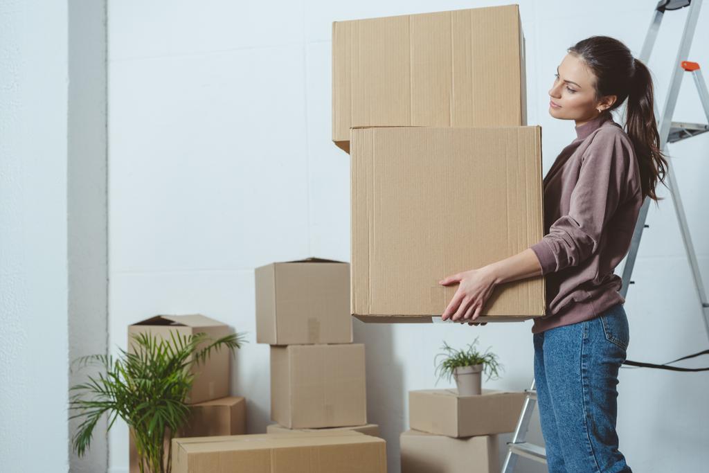 boční pohled na mladé ženy držící stoh krabic při stěhování - Fotografie, Obrázek